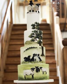 three tiered cake decorated with sheep and trees on the bottom layer, sitting in front of stairs