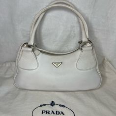 Prada Shoulder Bag By Miuccia Prada Vintage Sabbia Vitello Daino Leather Vitello Daino Leather & Enameled Metal Triangle Silver-Tone & Multitonal Hardware Rolled Handles Logo Jacquard Lining & Single Interior Pocket Zip Closure At Top Includes Authenticity Certificate **Prada Dust Bag Included** Estimated Item Measurements: Handle Drop: 8" Height: 7.25" Width: 13.5" Depth: 4.75" Color: White Please Look Closely At Each Pic And Angle To See Exact Condition & Dimensions. Flaws Noted: Loose Threads Where Handles Meet Bag; Minor Wear On Bottom Border Beading, A Couple Very Small Dark Spots (About The Size Of A Pen Point). Signs Of Wear/Use. Interior V Pre-owned Satchel Shoulder Bag, Pre-owned Luxury Formal Shoulder Bag, Luxury Pre-owned Shoulder Bag For Formal Occasions, Elegant Pre-owned Rectangular Bag, Pre-owned Elegant Leather Shoulder Bag, Pre-owned Elegant Top Handle Bag, Pre-owned Elegant Shoulder Bag For Shopping, Elegant Pre-owned Leather Shoulder Bag, Elegant Pre-owned Top Handle Bag