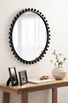 a table with a mirror, vase and pictures on it next to a wall mounted plant