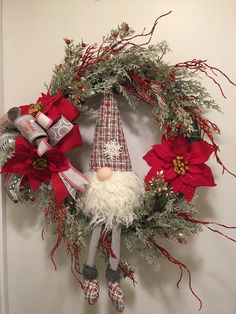 a christmas wreath with a gnome doll hanging from it's side and other decorations around it