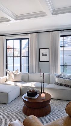 a living room filled with lots of furniture next to large window covered in white curtains