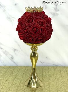 a gold vase filled with red roses and a crown on it's head, sitting on a table