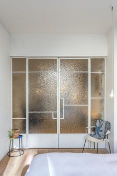 a bed sitting under a window next to a wall mounted glass paneled closet door