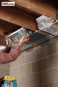 a man reading a magazine while hanging from a ceiling rack on a brick wall above a ladder