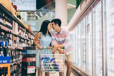 a man and woman kissing while pushing a shopping cart through a grocery store filled with drinks