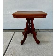 a small wooden table sitting on top of a cement floor next to a white wall