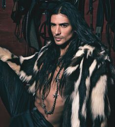 a man with long black hair wearing a fur coat and chain around his neck is posing for a photo