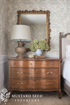 a bedroom with a dresser, mirror and lamp on it's side table in front of the bed