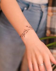 a woman's hand with a small tattoo on her left wrist and the other hand holding a plant