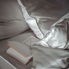 an open book sitting on top of a bed next to a satin covered comforter