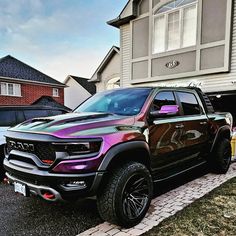 a black truck parked in front of a house with purple paint on it's hood