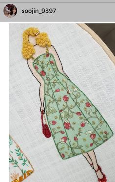 a woman in a green dress cross stitched on to a white piece of fabric