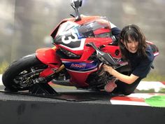 a woman kneeling down next to a red motorcycle