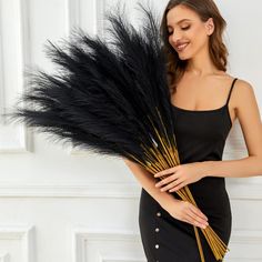 a woman in a black dress is holding some feathers