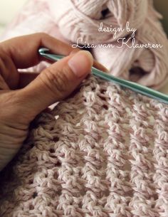 someone crocheting the stitches on a knitted blanket with a knitting needle and yarn ball in the background