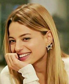 a woman with long blonde hair smiling and looking at the camera while wearing earrings