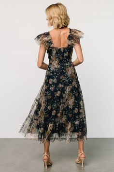 the back of a woman wearing a black floral print dress with sheer shoulders and ruffled sleeves