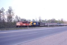 a train traveling down the tracks next to a road with trees in the background on a sunny day