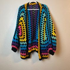 a multicolored crocheted sweater hanging on a wall next to a coat hanger