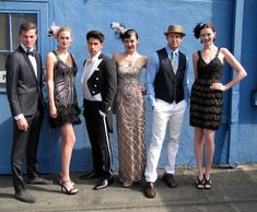 a group of people standing next to each other in front of a blue building wearing formal clothing