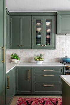 a kitchen with green cabinets and white counter tops, an area rug on the floor