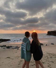 two people standing on the beach at sunset