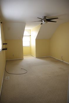 an empty room with a ceiling fan in the corner and no curtains on the windows