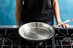 a person standing in front of an oven with a pan on the burner and cooking utensils