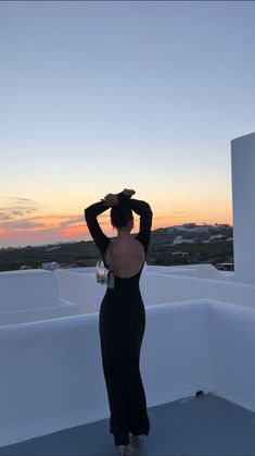 a woman standing on top of a roof with her back to the camera, wearing a black dress