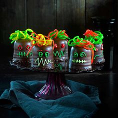 three decorated cakes sitting on top of a glass cake platter with neon colored icing