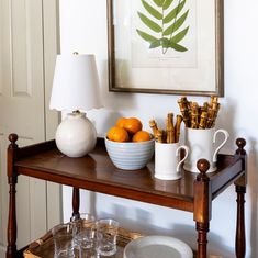 a wooden table topped with cups and bowls filled with oranges next to a painting