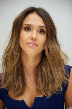 a woman with long brown hair wearing a blue dress and looking at the camera while standing in front of a white background