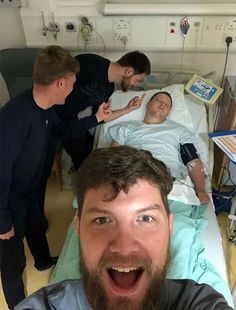 a man in a hospital bed with three other men around him and one is smiling