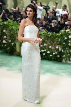 a woman in a strapless white gown standing on a runway with cameras around her