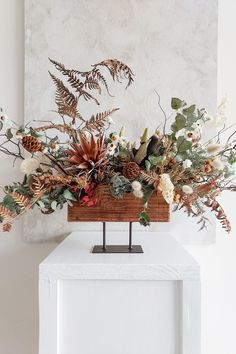 an arrangement of flowers and foliage in a wooden vase on a white table against a wall