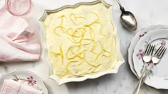 a cake with yellow icing sitting on top of a table next to plates and utensils