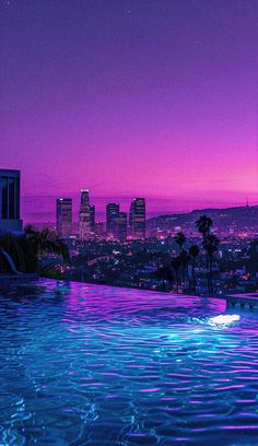 an empty swimming pool in front of a cityscape at night with the sun setting