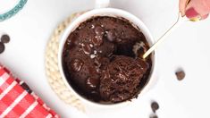 a person holding a spoon over a bowl of chocolate ice cream on a white table