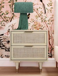 a white dresser with two drawers and a green lamp on top of it in front of a pink wall