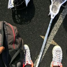 two pairs of shoes and backpacks on the ground with lacrosse sticks attached to them