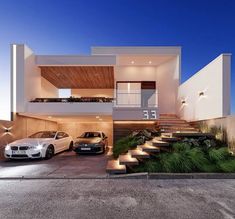 two cars are parked in front of a modern house at night with stairs leading up to the upper floor