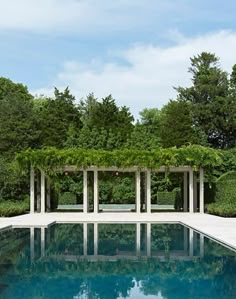 an empty pool surrounded by greenery and white pillars with benches on each side in front of it