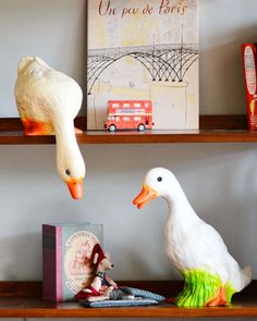 two white ducks are sitting on bookshelves next to some books and other items