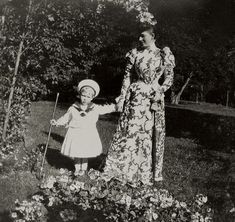 an old black and white photo of two women standing in the grass with flowers on their head