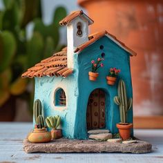 a small blue house with cactus and succulents on the roof is sitting on a table