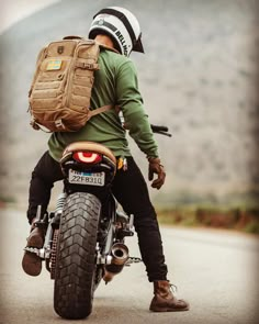 a man riding on the back of a motorcycle down a road with a backpack strapped to it's back