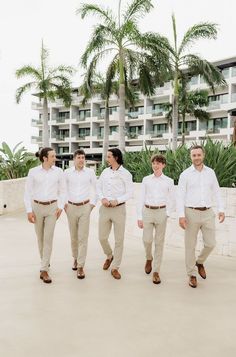 a group of men standing next to each other on top of a cement floor near palm trees