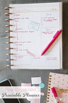 an organized planner with pink and gold accents on a gray surface next to a cell phone