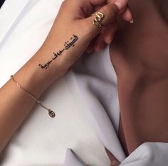 a woman's arm with arabic writing on it and a gold chain around her wrist