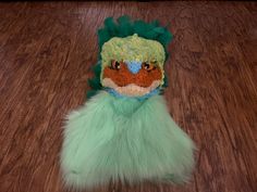 a stuffed animal with green fur on top of a wooden floor next to a brown table